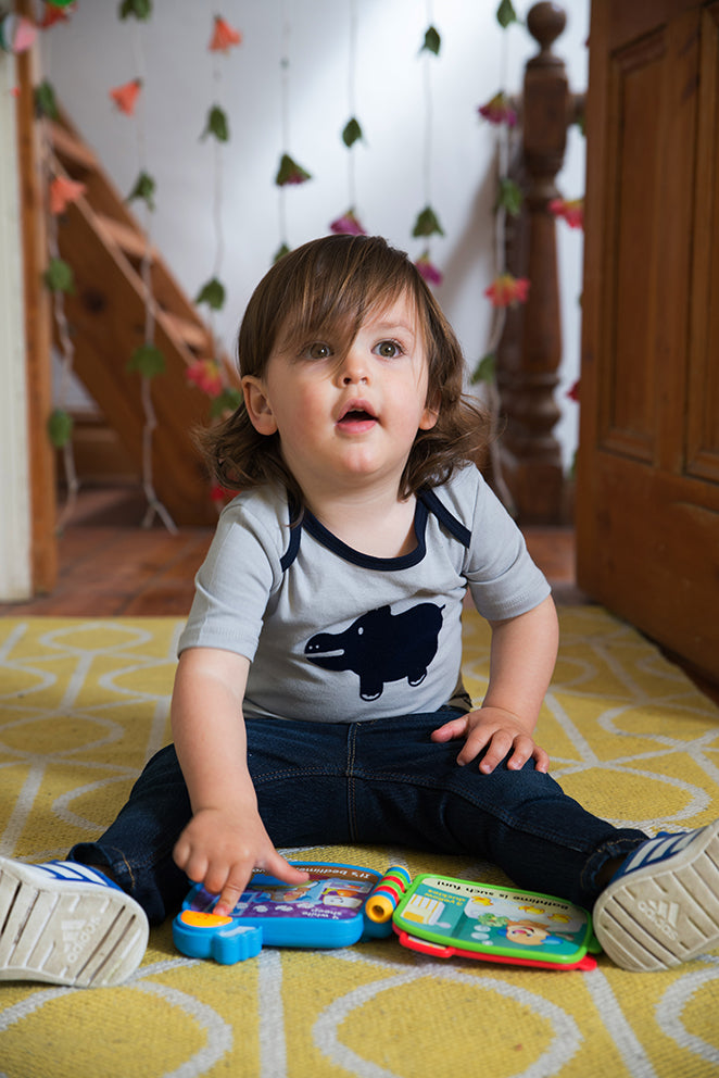Child sitting on a yellow rug with toys, surrounded by wooden furniture and decorative items.